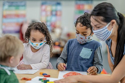 daycare Photo of a teacher and preschool aged children in a classroom wearing face masks
