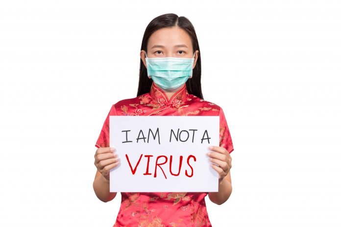 Asian woman in Chinese costume wear a hygienic mask holding sign I am not a VIRUS for anti racism , bullying and hate in the outbreak situation of Coronavirus 2019 infection or Covid-19 Photo of an Asian woman wearing a face mask and holding a sign that says