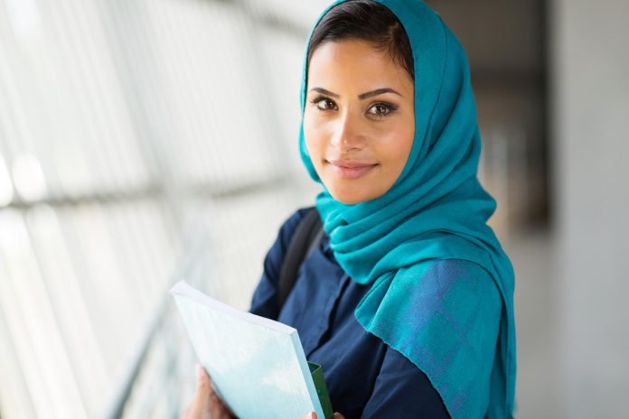 Islamic college student holds a book while looking into camera