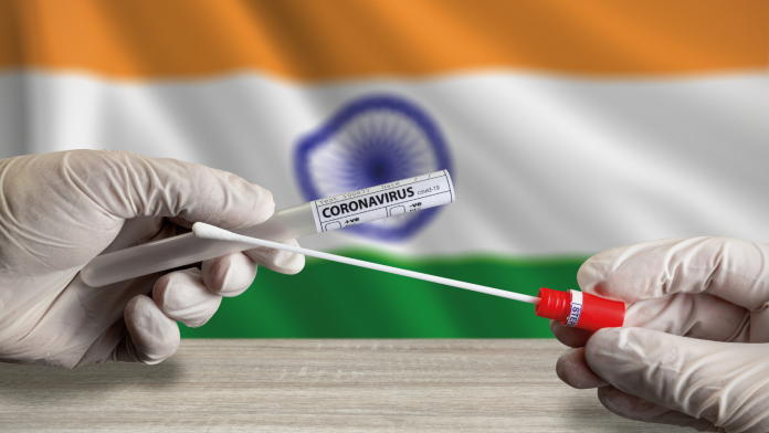 covid19-india Photo of gloved hands holding a COVID-19 test in front of an Indian flag.